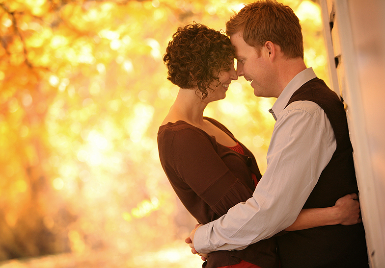 engaged couple embracing against a wall with orange yellow leaves in the background