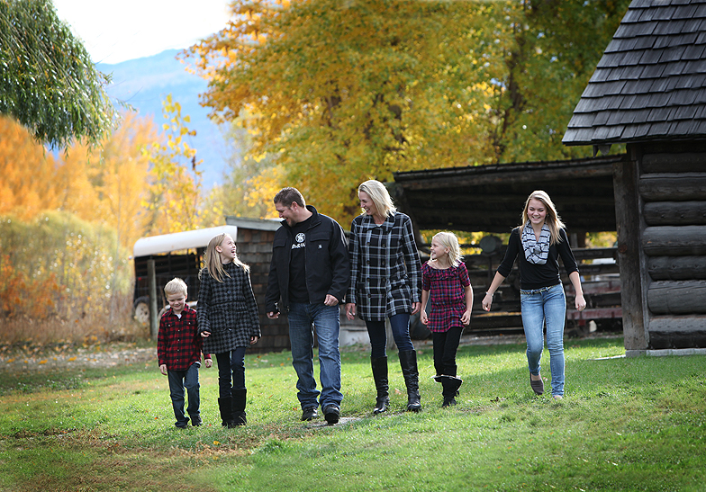 family of 6 wearing dark colours walking in a line in a farm yard with fall leaves