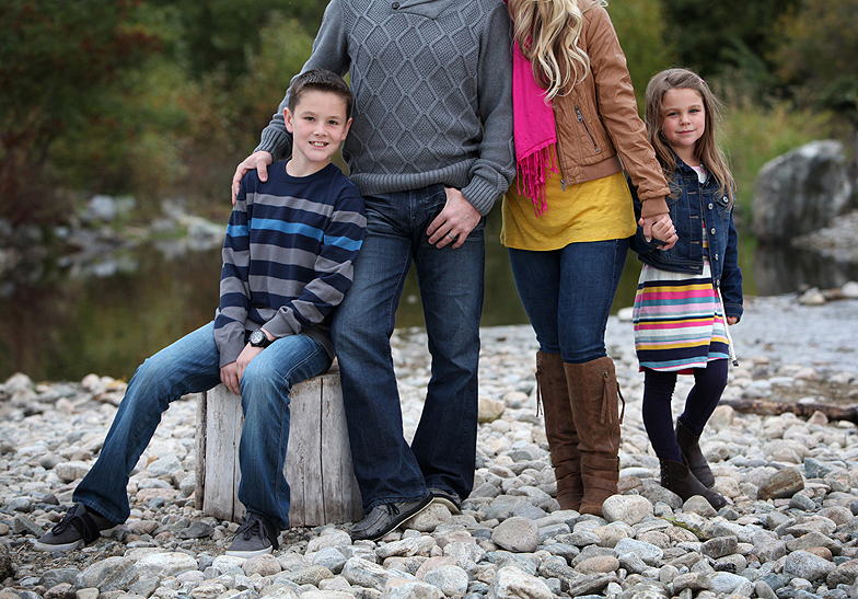 family of 4 standing on a rocky beach, cropped out parents with focus on kids in stripped outfits