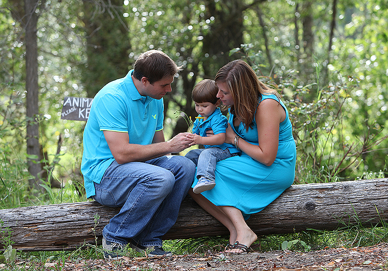 family of 3 wearing blue and jeans sitting on a log in the forest