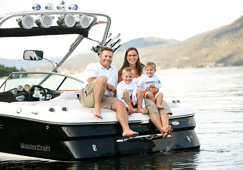 family of 4 wearing white t-shirts sitting on a boat on the lake by mountains