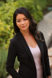 Business Portrait of a black haired woman wearing a black jacket and pink top in a garden setting