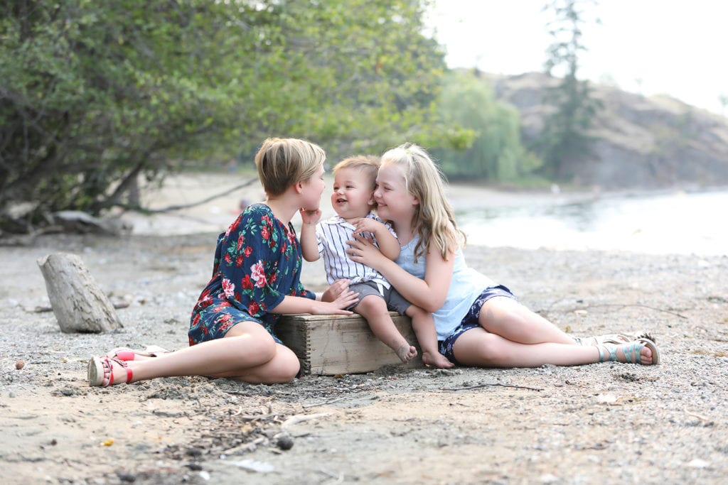 3 siblings sitting and laughing on a beach