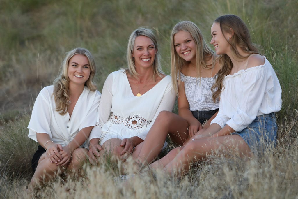 mother and daughters wearing white sitting in a field of dried grass