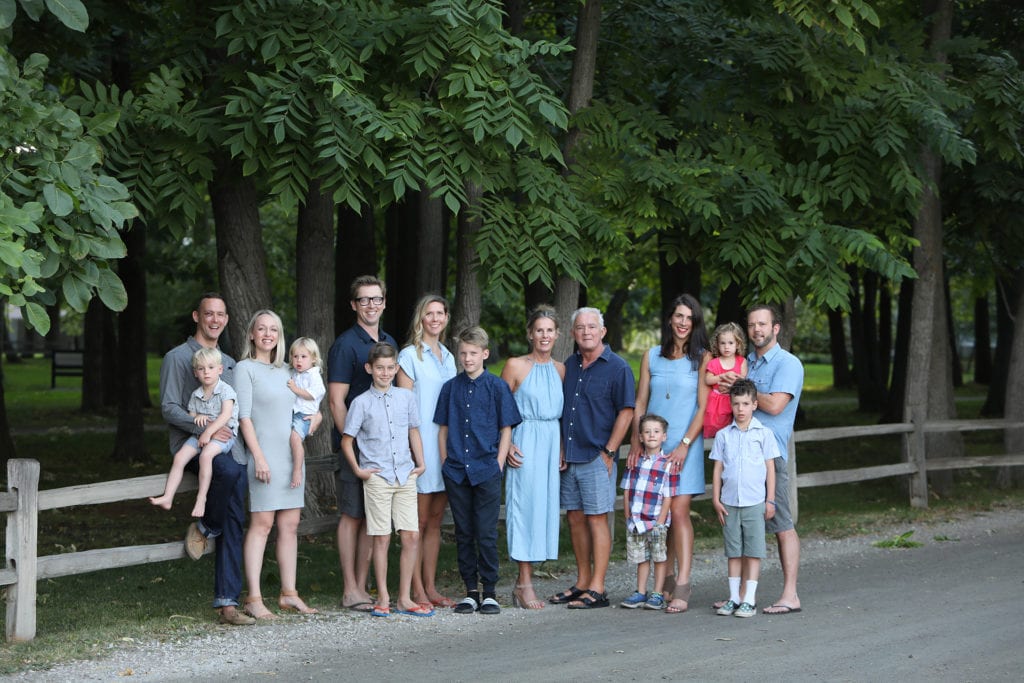 large family portrait standing by a rustic fence by a road and forest one child wears a red dress