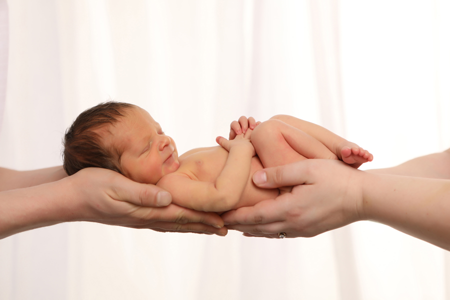 Newborn sleeping in parents hands against white curtains