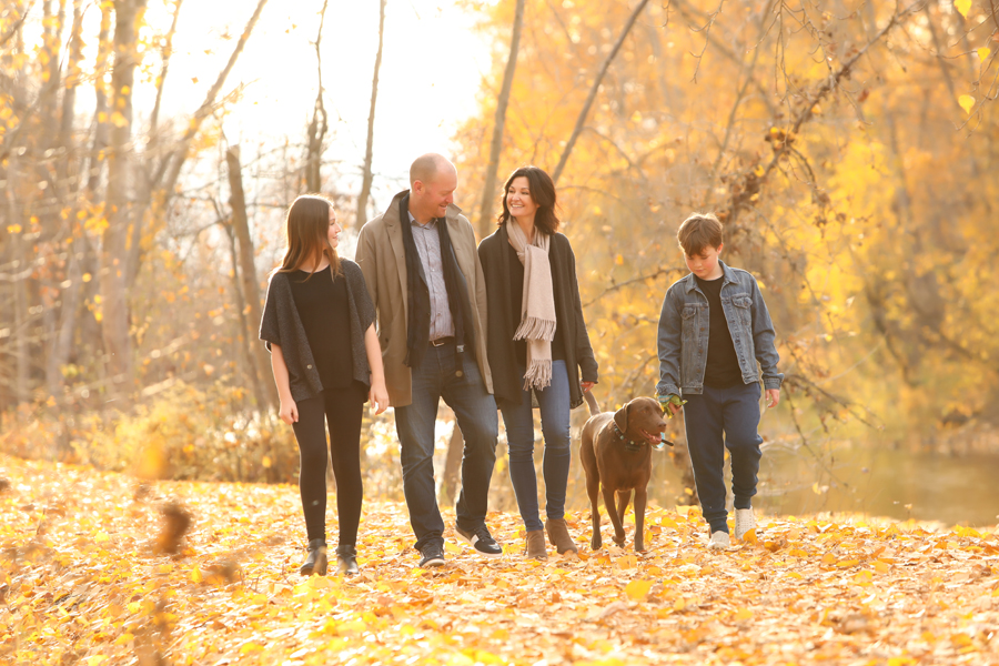 family of 4 walk with dog on a path of orange autumn leaves in a forest